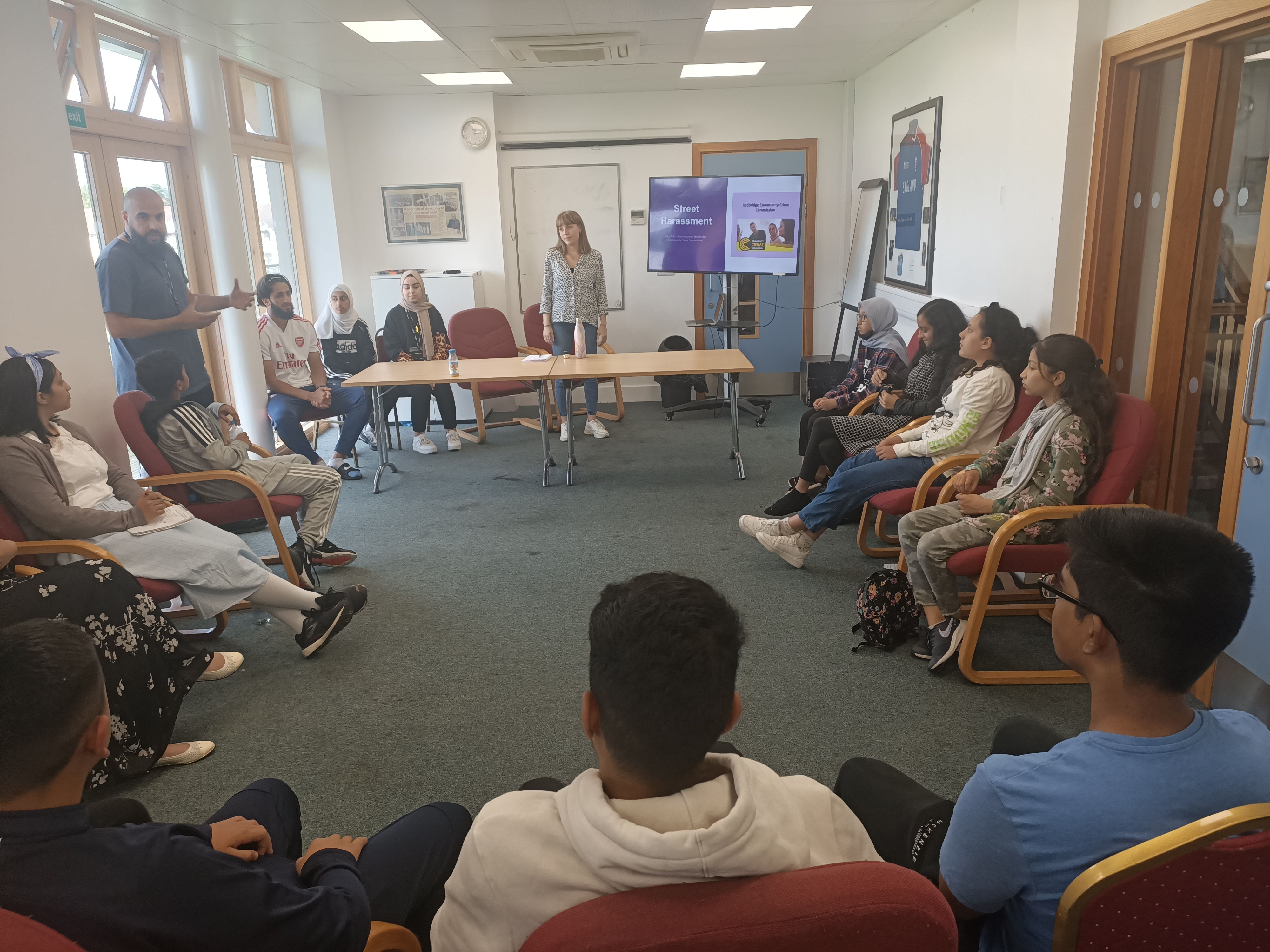 Children are sat on chairs in a semi circle looking at people speak at the front